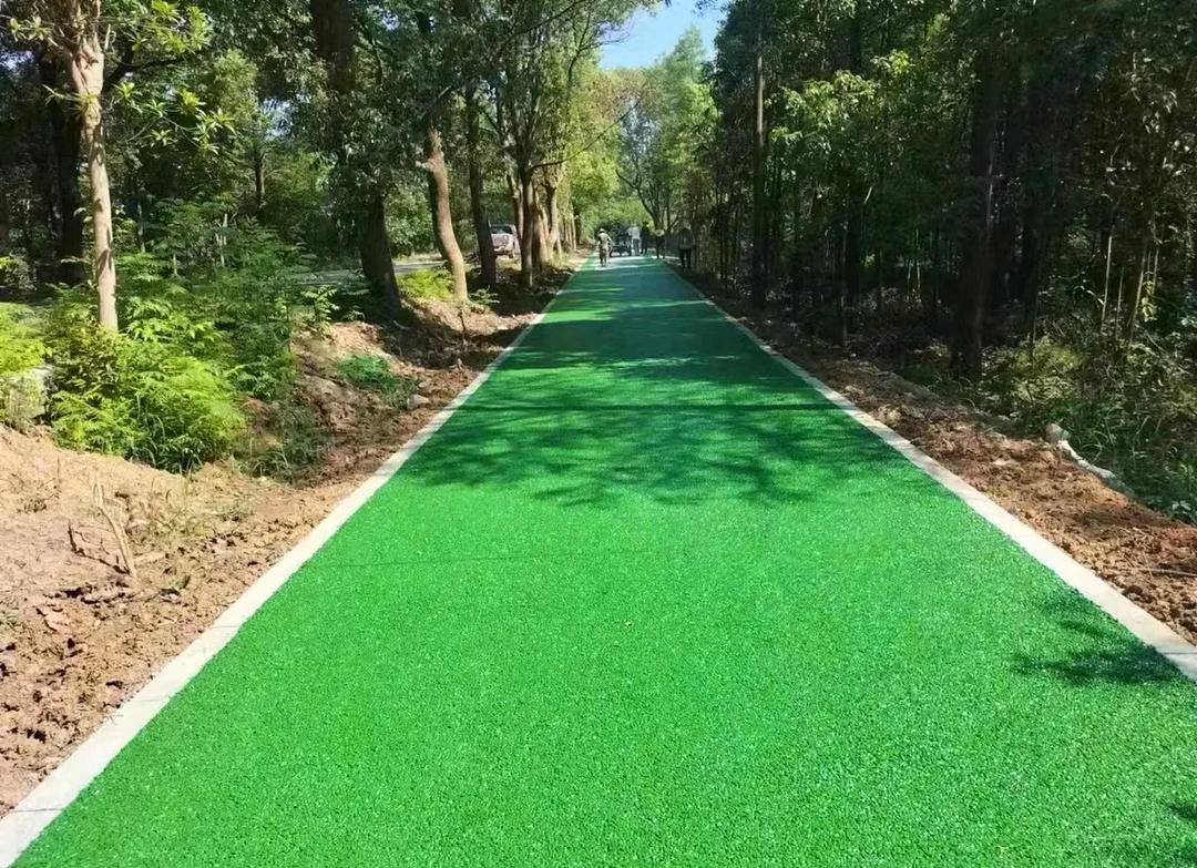 A vibrant green permeable concrete pathway stretches through a sun-dappled forest, bordered by white edge lines and flanked by dense trees casting dappled shadows on the surface. A vibrant green permeable concrete pathway stretches through a sun-dappled forest, bordered by white edge lines and flanked by dense trees casting dappled shadows on the surface.