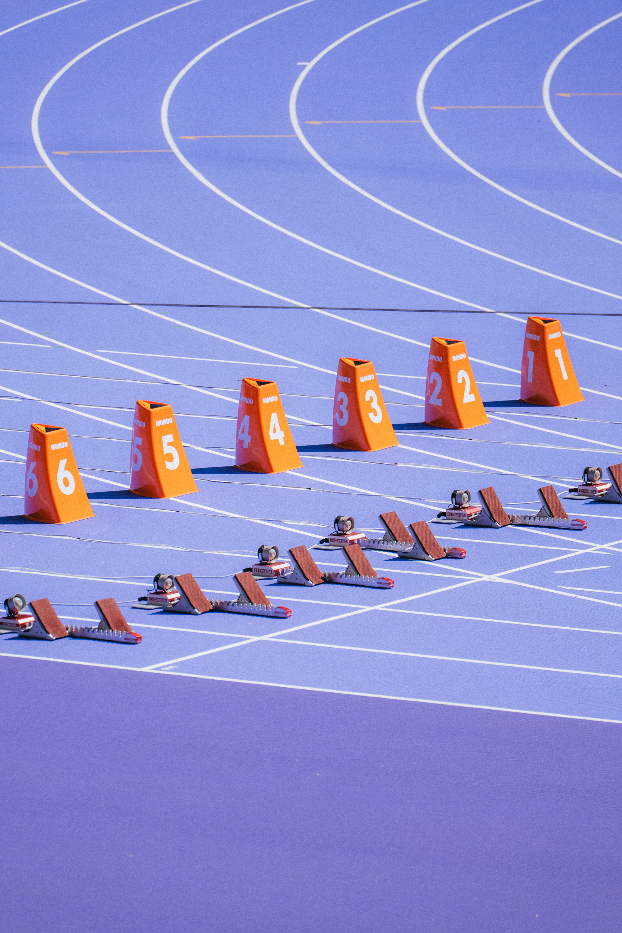 Un primer plano de la pista de atletismo violeta en el Estadio de Francia durante los Juegos Olímpicos de París 2024, con bloques de salida de color naranja numerados del 1 al 6 alineados en los carriles curvos: los primeros Juegos Olímpicos.