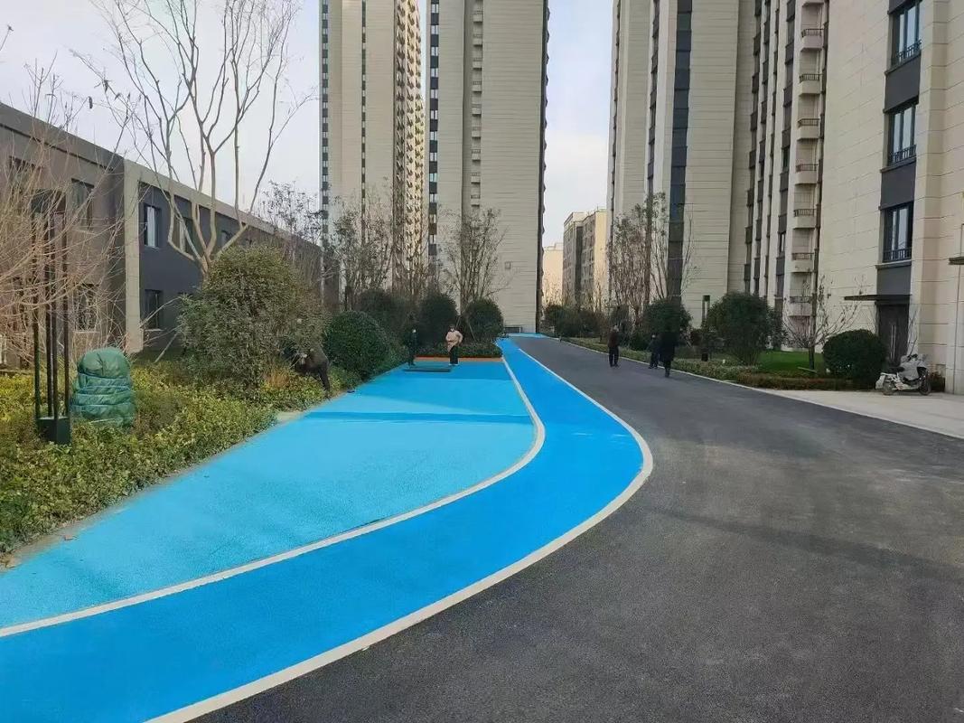 A vibrant blue running track winding through a modern residential complex, flanked by high-rise apartment buildings and landscaped greenery under an overcast sky. A vibrant blue running track winding through a modern residential complex, flanked by high-rise apartment buildings and landscaped greenery under an overcast sky.