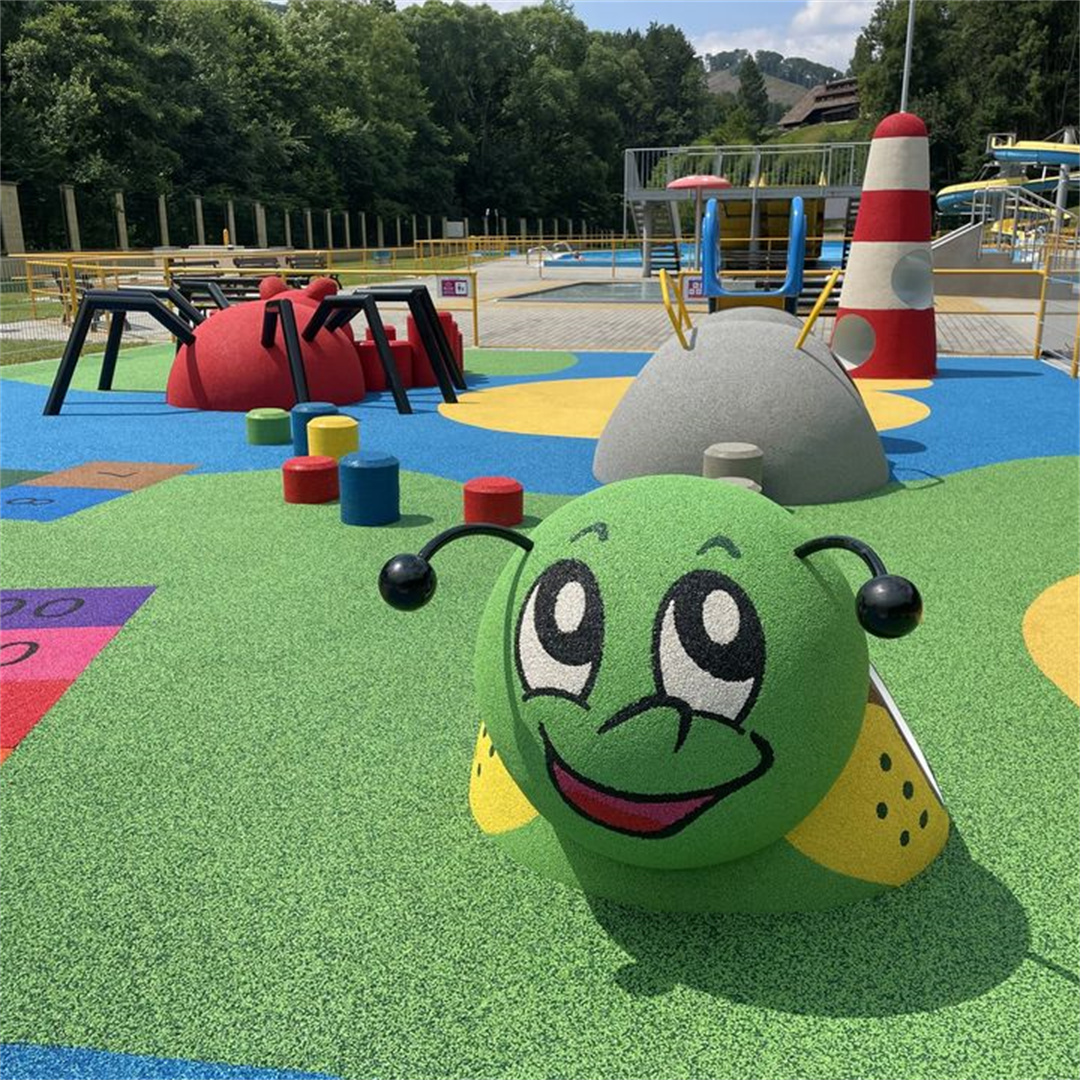 A vibrant outdoor children’s playground featuring colorful EPDM rubber flooring in green, blue, and yellow, with whimsical play structures — including a smiling green caterpillar, a red spider