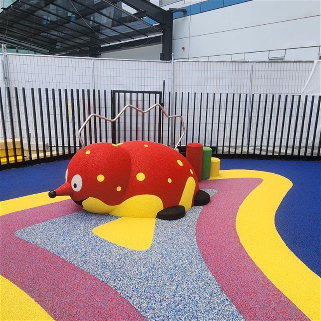 A vibrant indoor children’s play area featuring colorful EPDM rubber flooring in blue, yellow, and magenta, with a whimsical red-and-yellow ladybug-shaped play structure designed for safe, eng