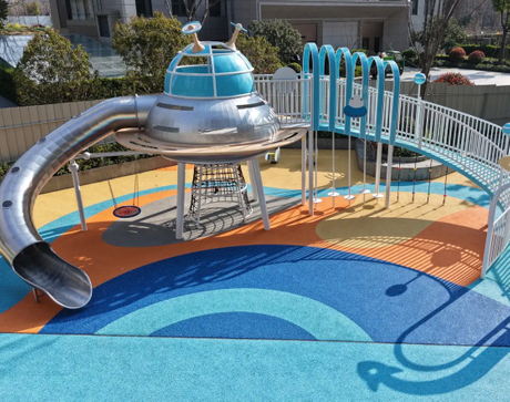 A playground featuring a metallic UFO - shaped slide structure, with the ground covered in colorful EPDM rubber granules in shades of blue, orange, and yellow, providing a safe and vibrant play surf.jpeg