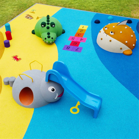 A vibrant EPDM rubber playground surface in yellow and blue, featuring playful animal-shaped play structures — including a green dinosaur, a gray elephant slide, and a spotted orange creature.jpg