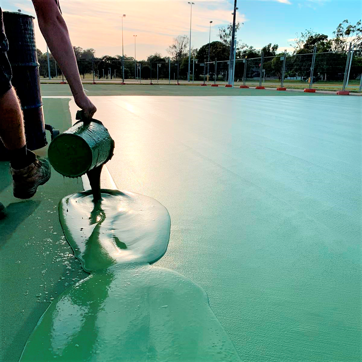 Worker pouring green Silicon PU coating, highlighting smooth flow & seamless application for courts.