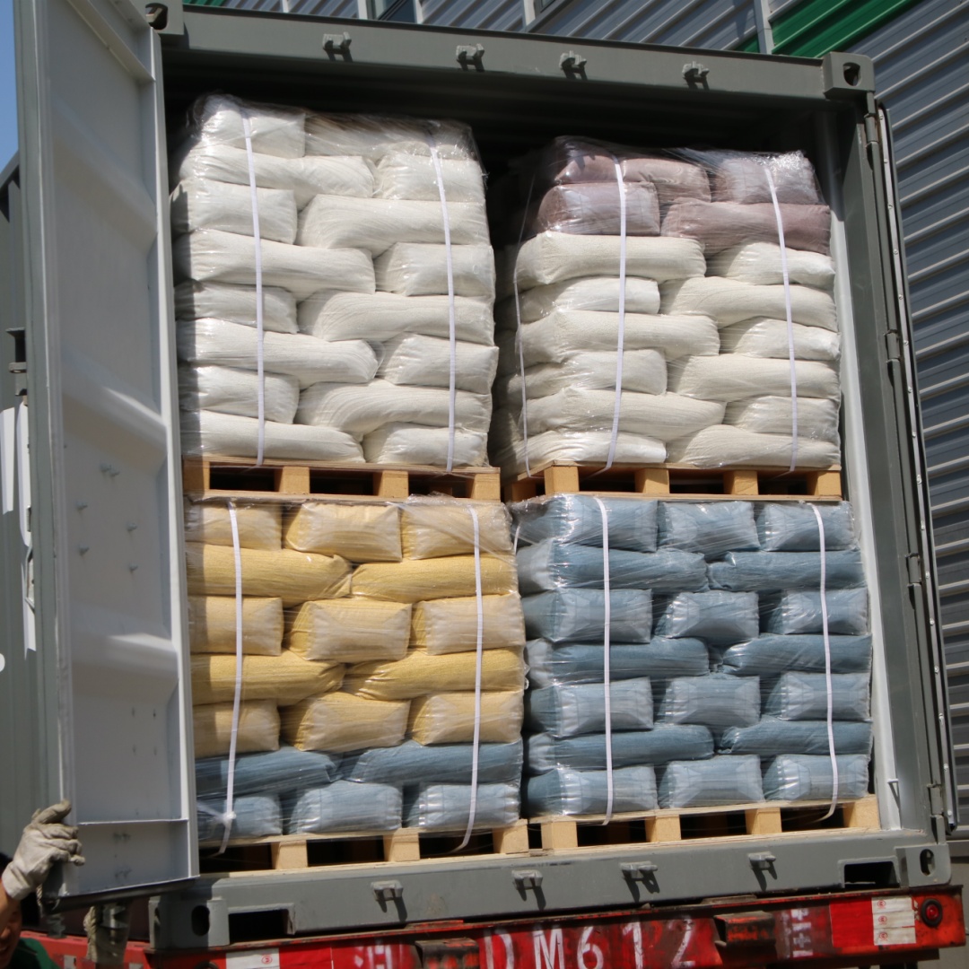 An open shipping container loaded with pallets of bagged industrial materials, including white, yellow, and blue sacks wrapped in plastic and secured with straps, ready for transport.