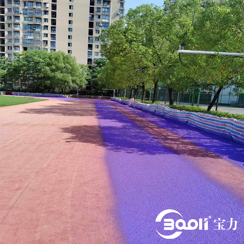 Яркая фиолетово-красная беговая дорожка из гранул EPDM изгибается через обсаженный деревьями городской парк на фоне высотных жилых зданий, демонстрируя современный, красочный и прочный вид.