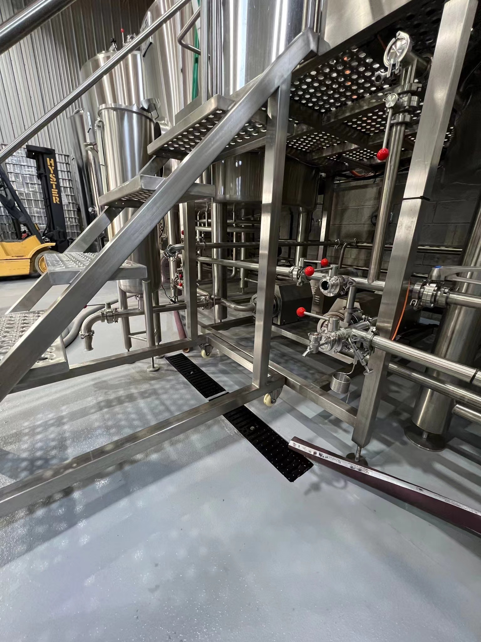 A polyurea-coated industrial floor in a stainless steel processing facility, featuring seamless gray flooring beneath metal staircases and piping systems, demonstrating polyurea’s application in